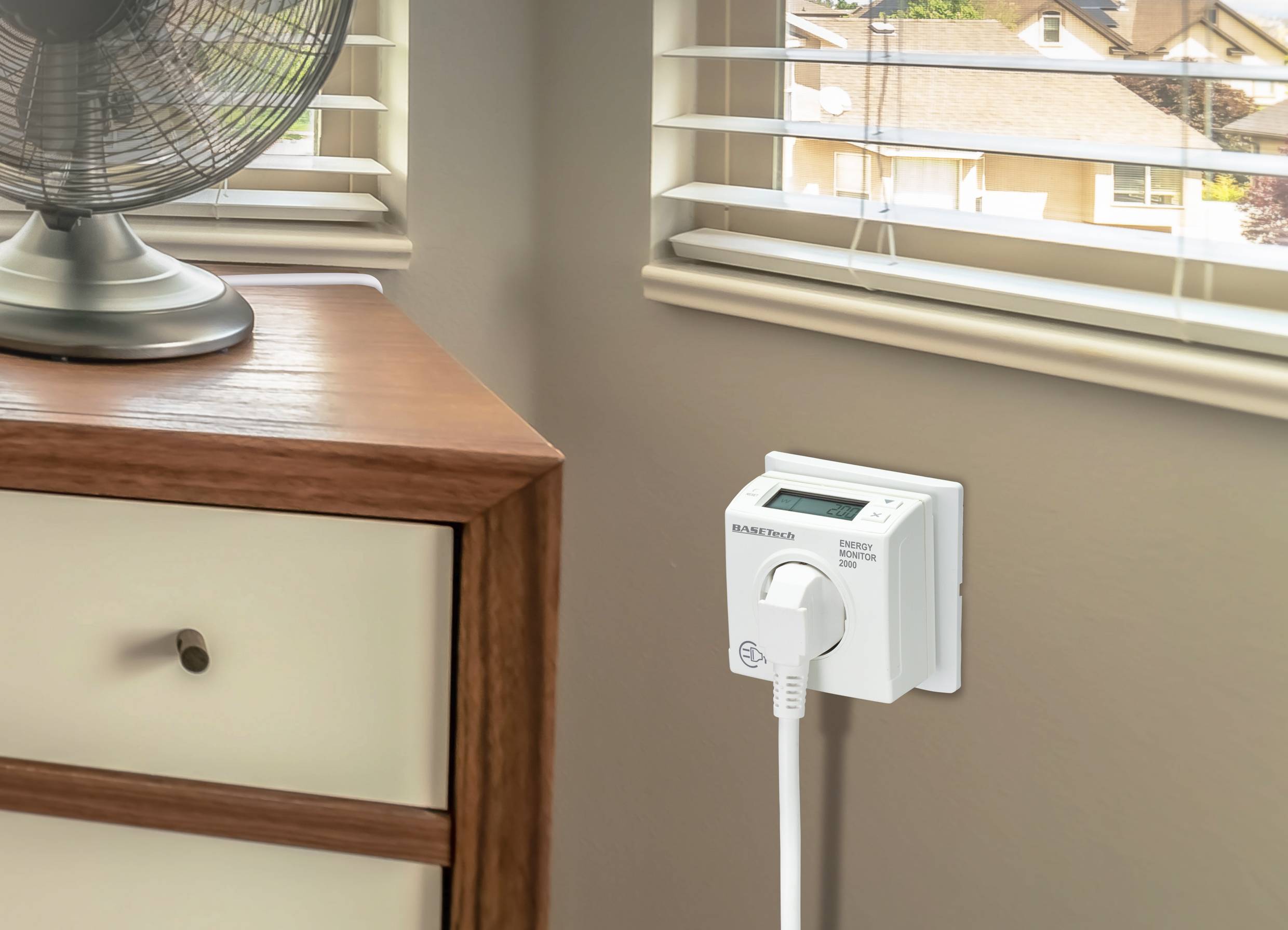 Een elektrische temperatuurschakelaar is aangesloten op een stopcontact in een zonovergoten ruimte, naast een commode met ventilator.