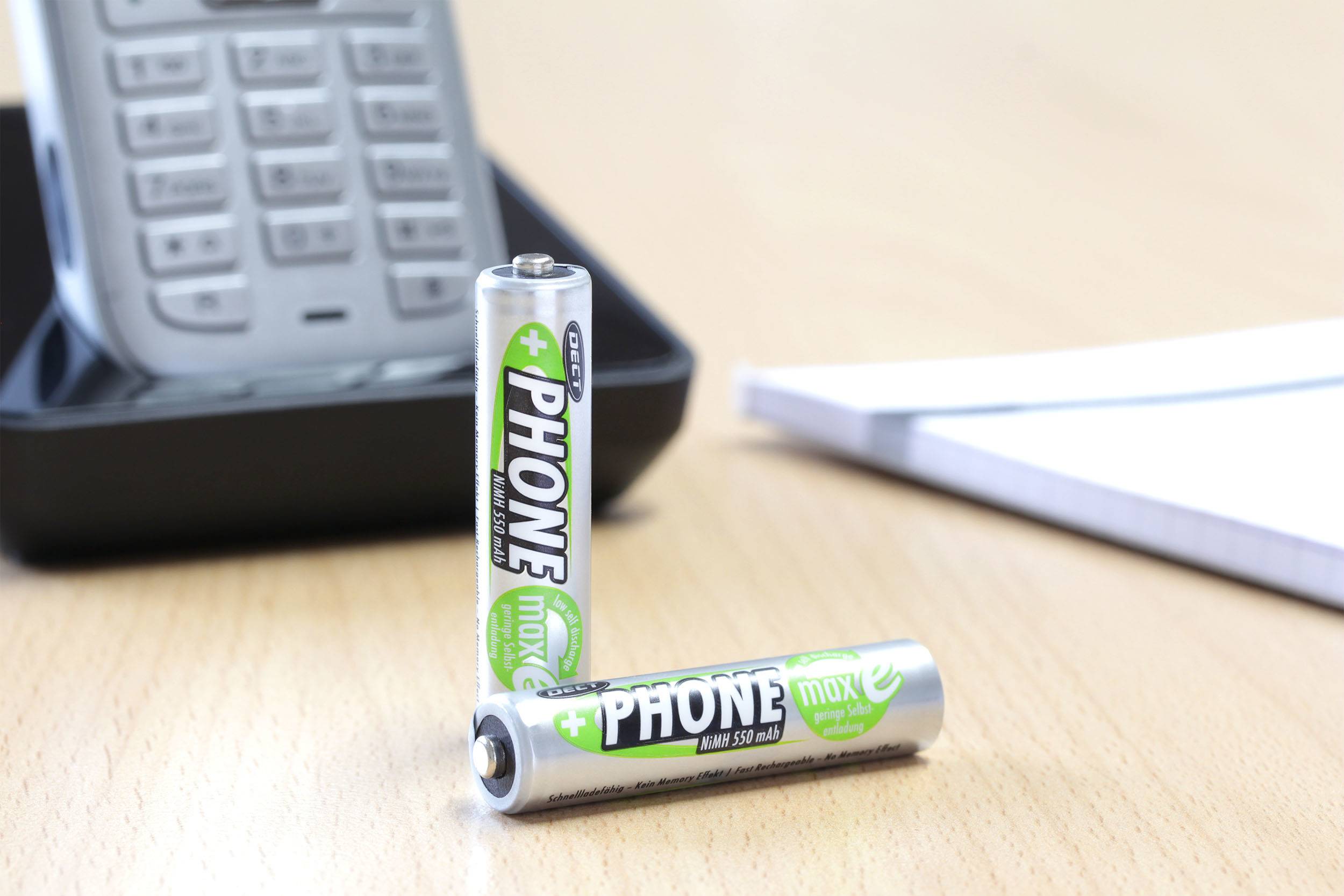 Twee batterijen staan voor een draadloze telefoon op een tafel. Op de achtergrond ligt een notitieblok.