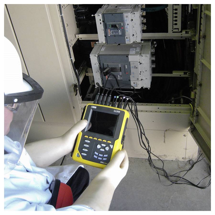 Een persoon voert veiligheidstests uit op elektrische apparaten en gebruikt een geel meetapparaat terwijl hij beschermende uitrusting draagt.