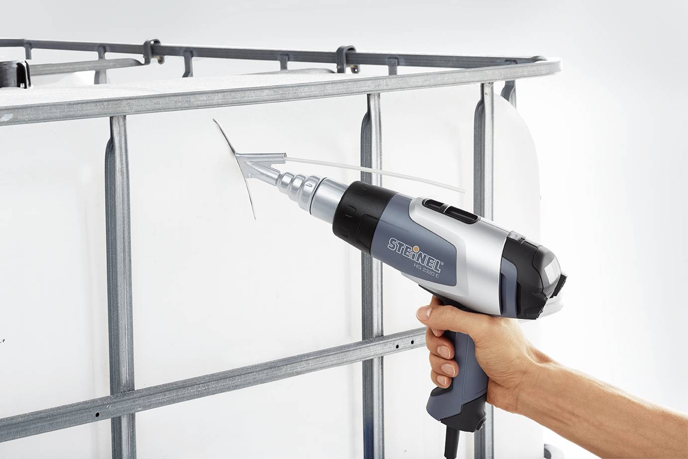 Een hand houdt een elektrische bouten- en staafsnijder vast, die een metalen staaf aan een steiger doorsnijdt. Het apparaat heeft een blauw-grijs behuizing.