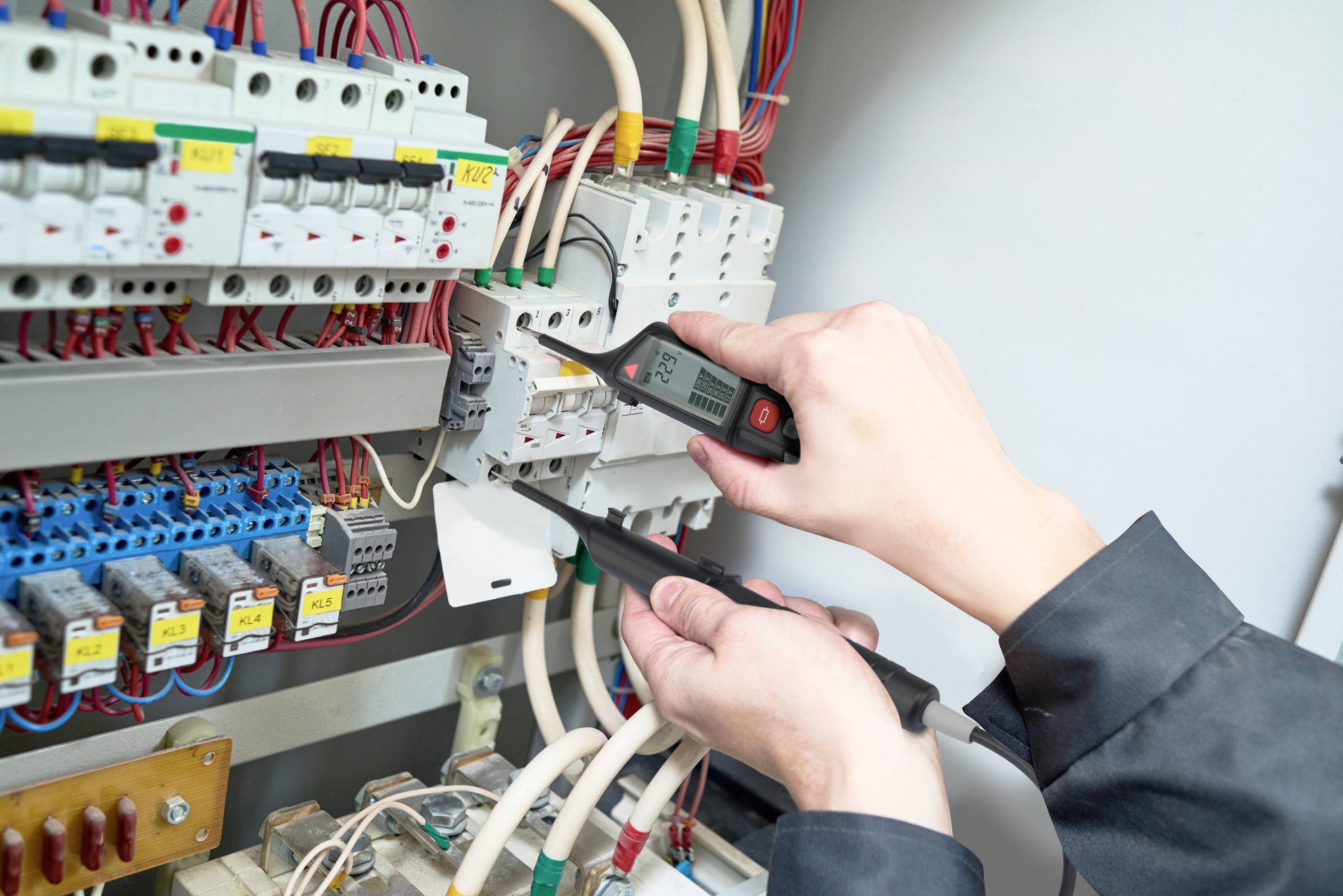 Een persoon controleert elektrische zekeringen in een verdeelkast met behulp van een testapparaat. De scène toont zorgvuldigheid en techniek.