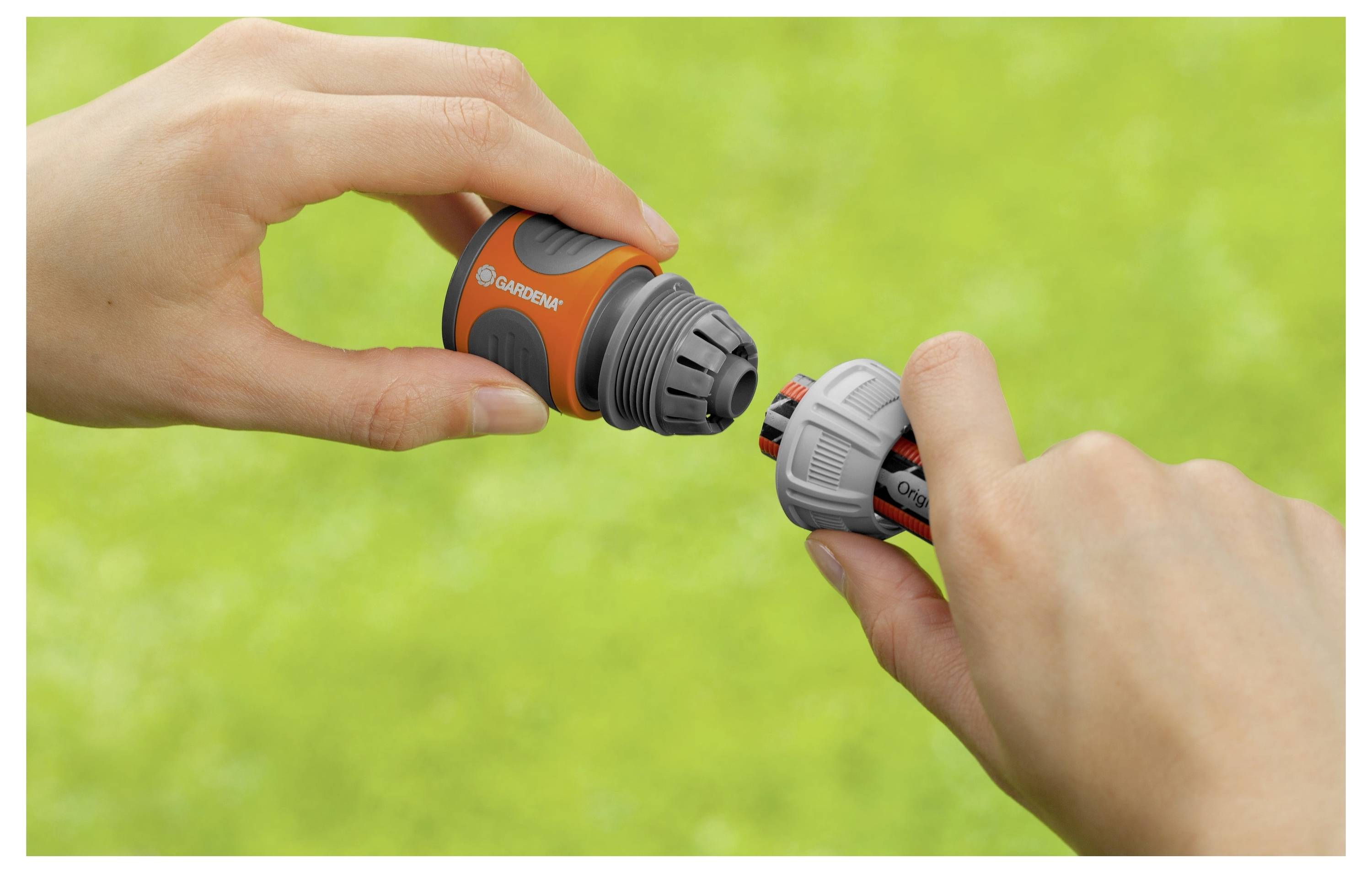 Handen die een tuinslang met een oranje en grijze spuitkop tegen een groene gazonachtergrond verbinden.