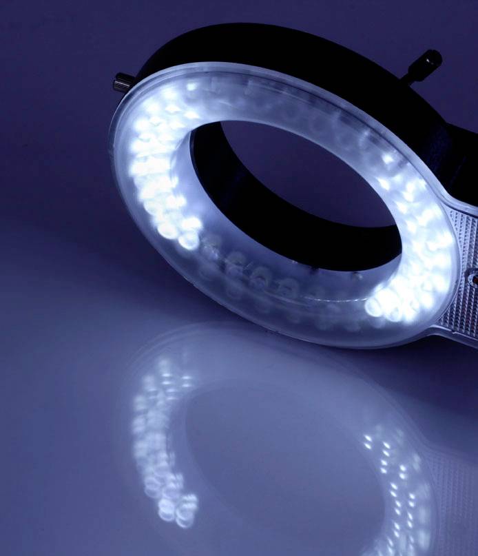 Een ringlicht met stralend wit LED-licht rust op een spiegelend oppervlak, waarbij het licht een cirkelvormige reflectie creëert.