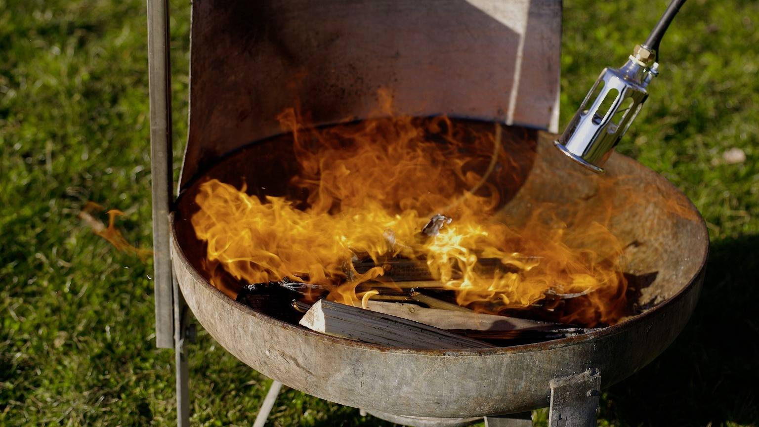 Een ronde vuurkorf buitenshuis met brandend hout. Een vlam van een brander wordt toegevoegd om het vuur te versterken.