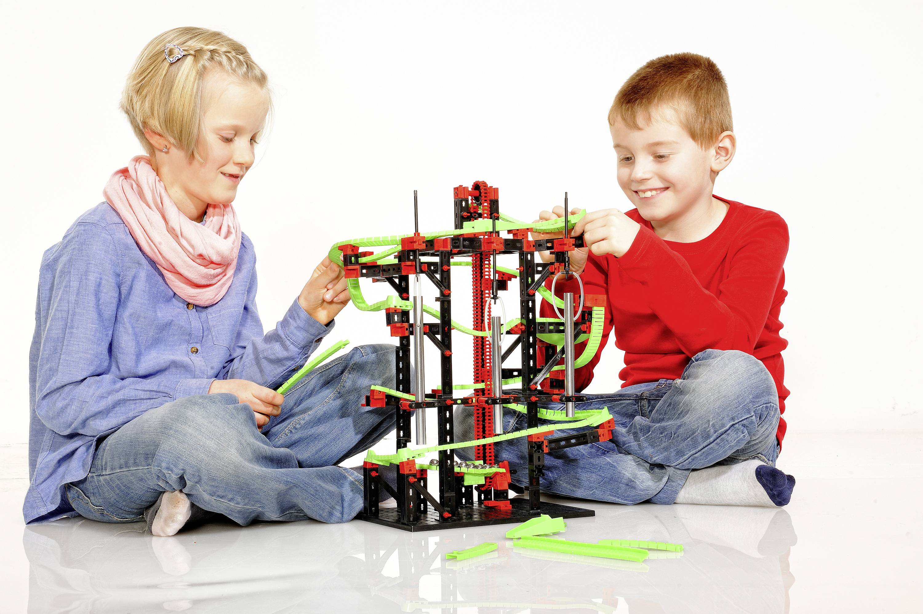 Twee kinderen bouwen samen een constructiespeelgoed-model uit kleurrijke onderdelen. Ze zitten op de grond en glimlachen.