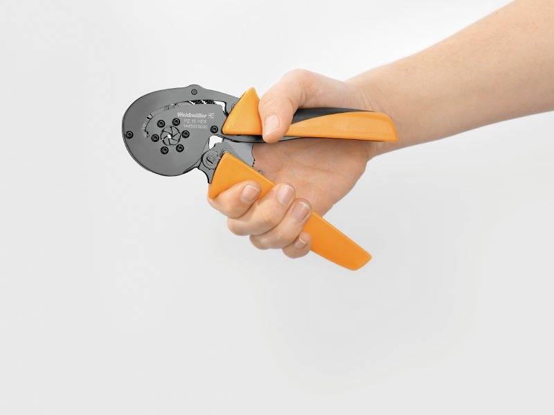 Een hand houdt een oranje-zwarte krimptang vast, geschikt voor elektrische verbindingen.