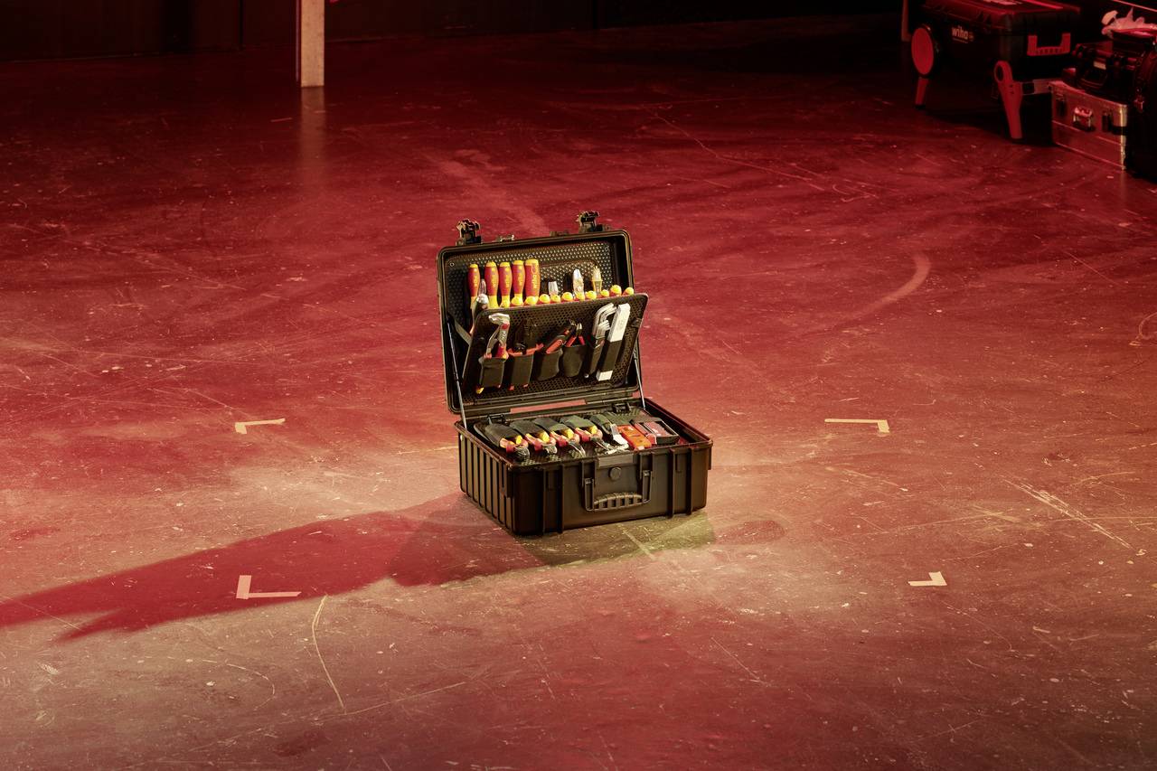 'Een open gereedschapskist met verschillende gereedschappen, zoals schroevendraaiers en tangen, staat op een podium met rood licht.'