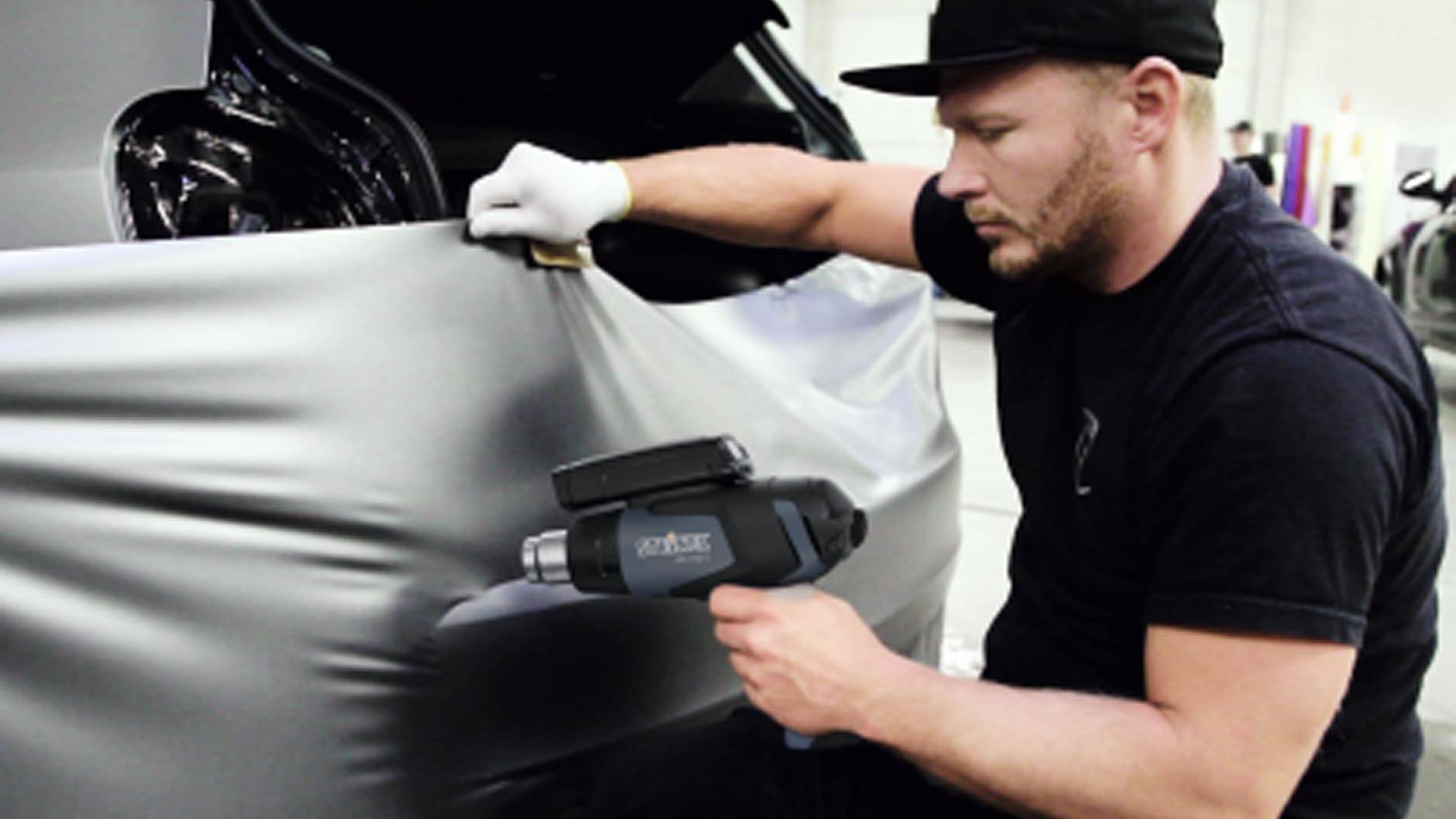 Een persoon die een auto-bekleding aanbrengt, houdt met één hand de folie vast en verwarmt deze met een heteluchtpistool.