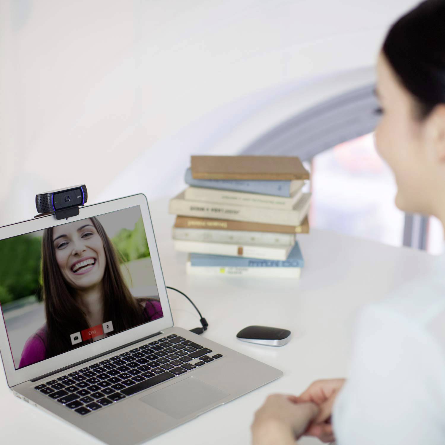 Een persoon neemt deel aan een videoconferentiegesprek op een laptop. Een stapel boeken is zichtbaar op de achtergrond.