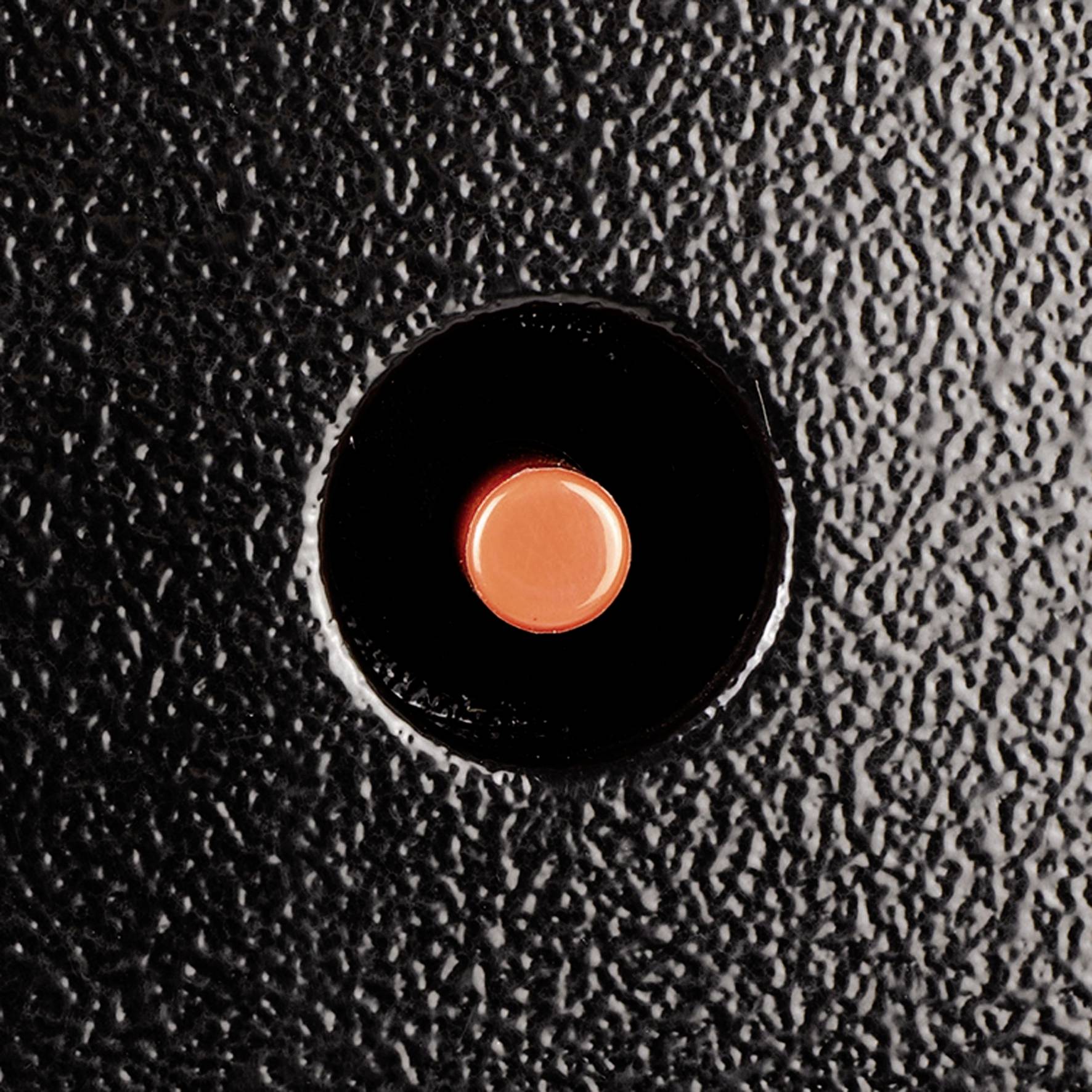 Een rode knop op een zwart oppervlak met een gestructureerde uitstraling, centraal geplaatst.