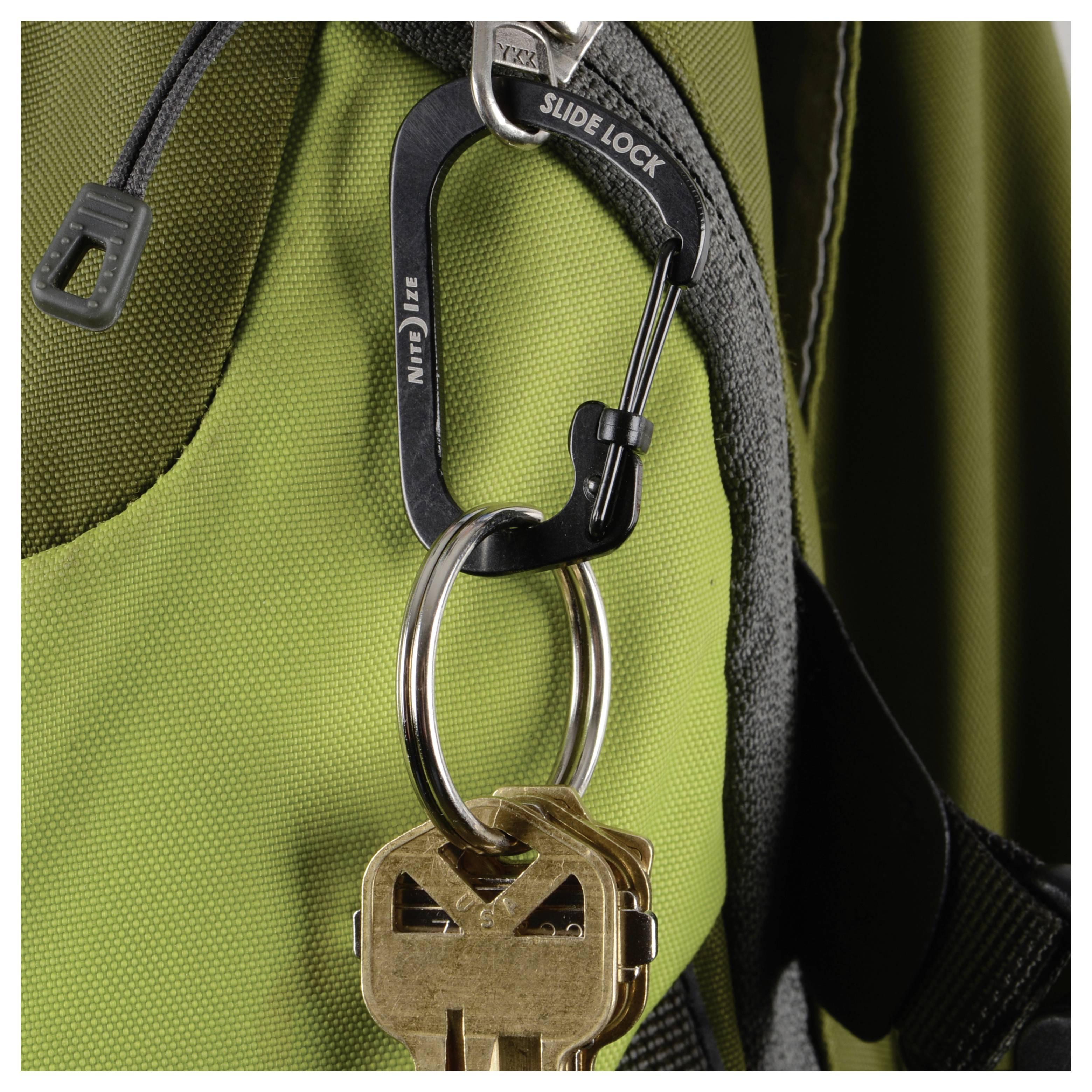 Een karabijnhaak met het label 'Slide Lock' houdt twee sleutels vast aan een rugzakriem.
