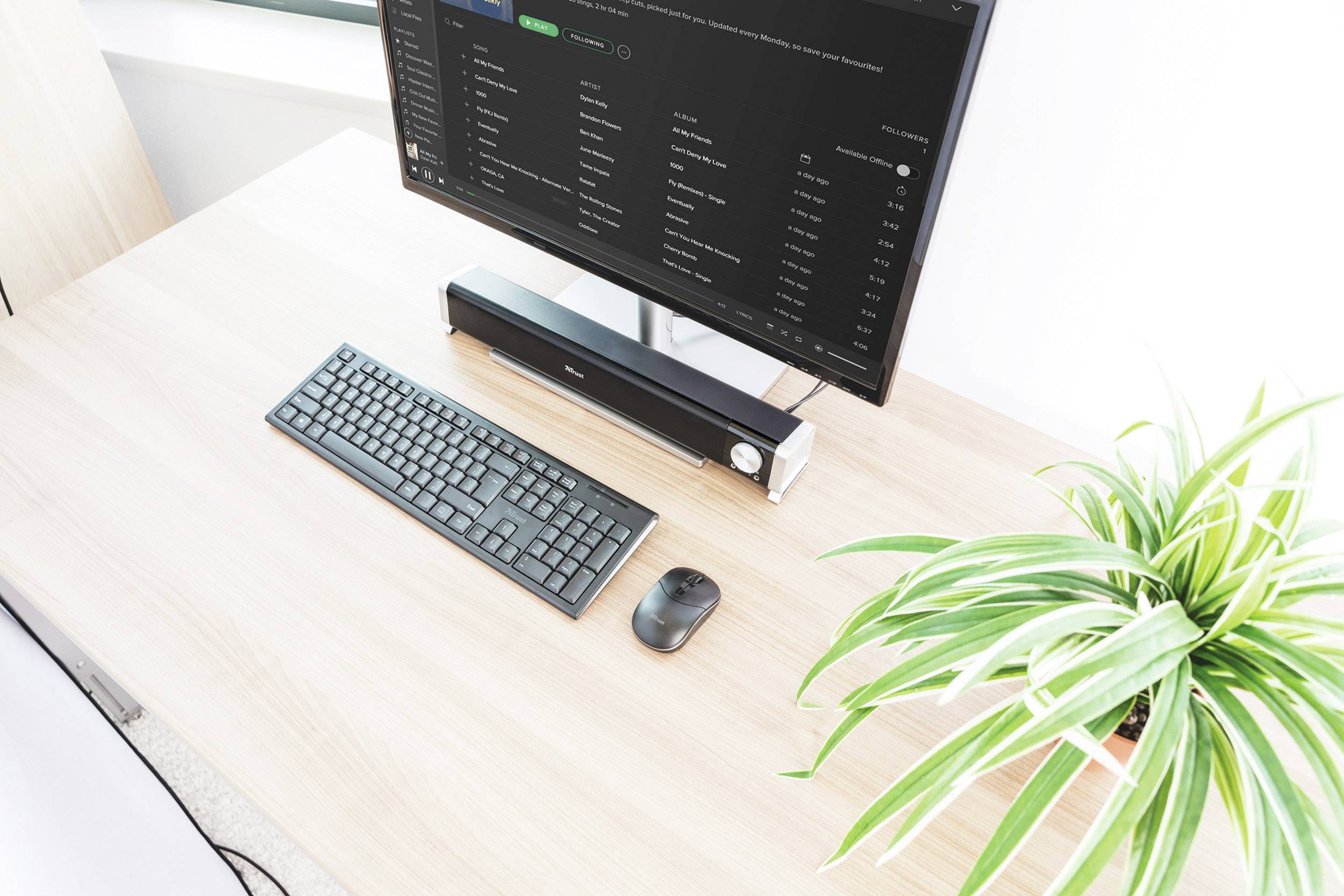 Een moderne bureau met een computerscherm, toetsenbord, muis en een kamerplant aan de rechterkant.