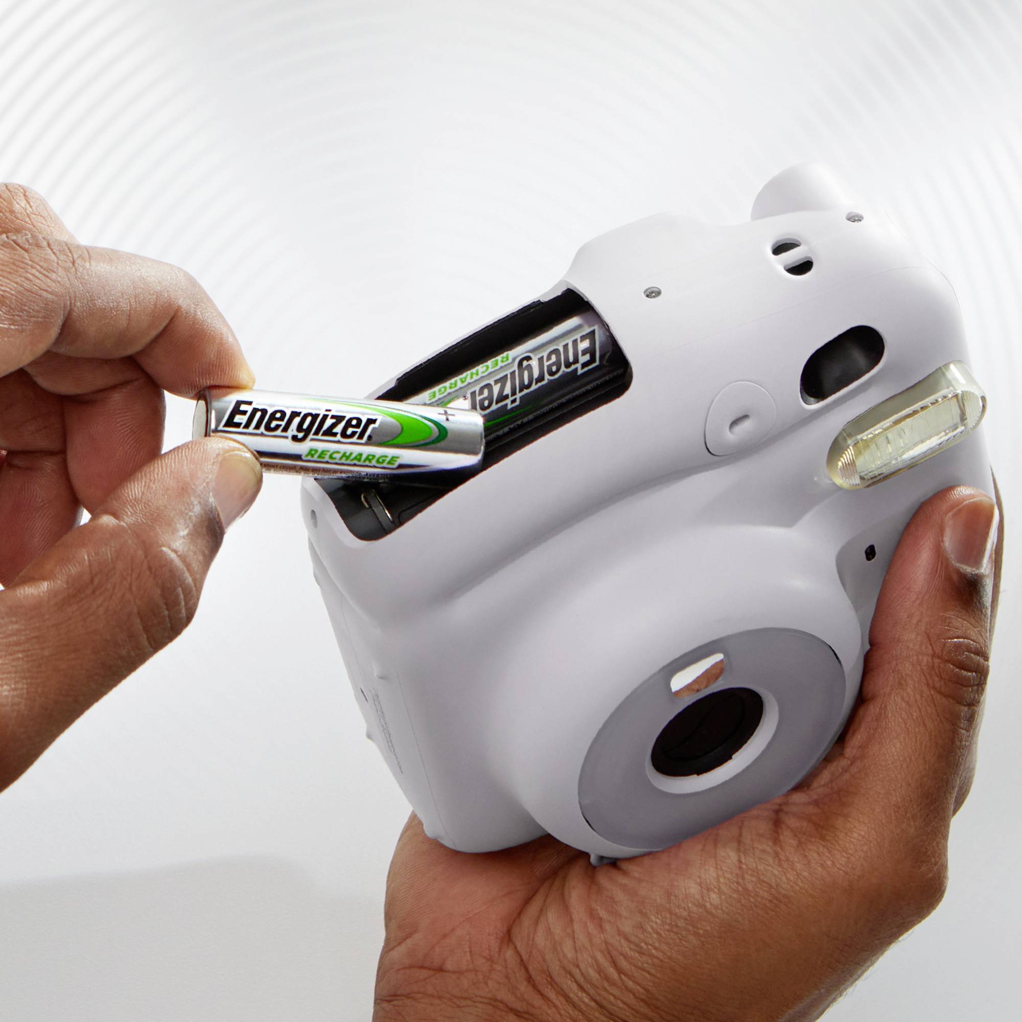Een hand plaatst een 'Energizer'-batterij in de achterkant van een witte camera om deze van stroom te voorzien.