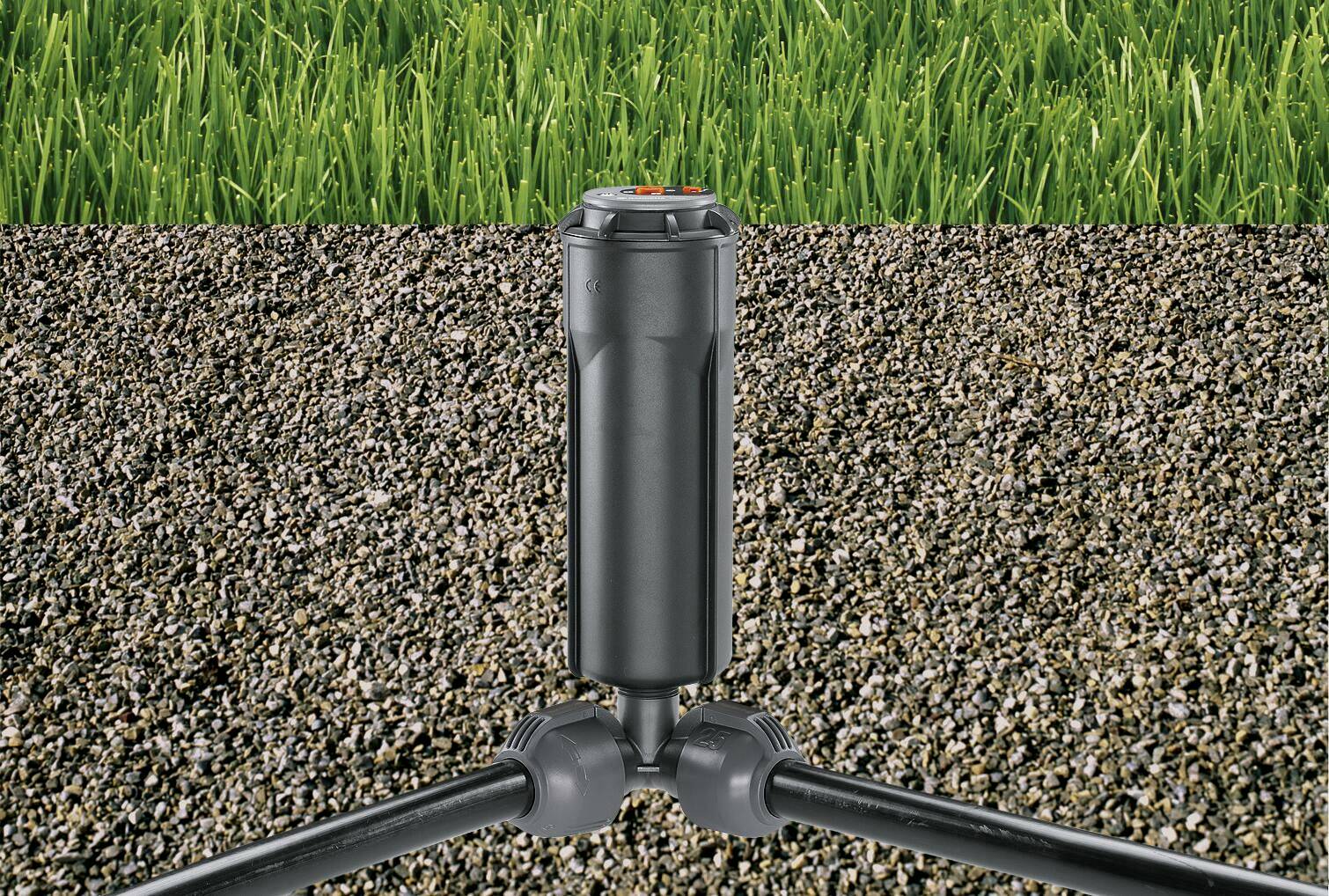 Een automatische sproeier met zwarte buizen is in de grond geïnstalleerd, hij steekt boven de bodem uit, met gras op de achtergrond.