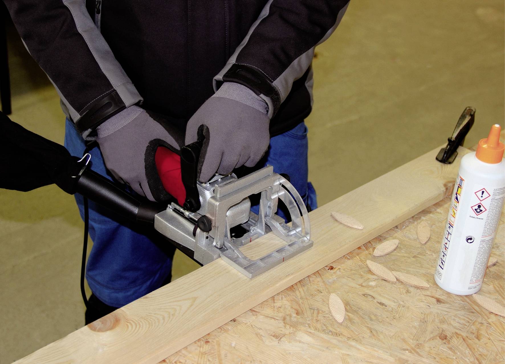 Een persoon gebruikt een houtbewerkingsmachine op een plank. Ernaast liggen houten pluggen en een flesje lijm.