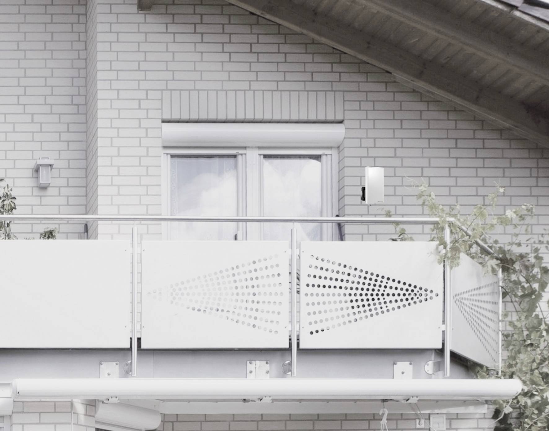 Een wit balkon met moderne leuningen en een versierde voorgevel aan een bakstenen huis. Een raam met een neergelaten rolluik op de achtergrond.