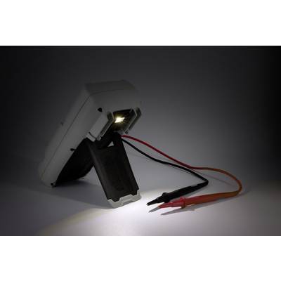Een multimeter met verlicht display ligt op een oppervlak. Twee meetkabels in rood en zwart steken uit.
