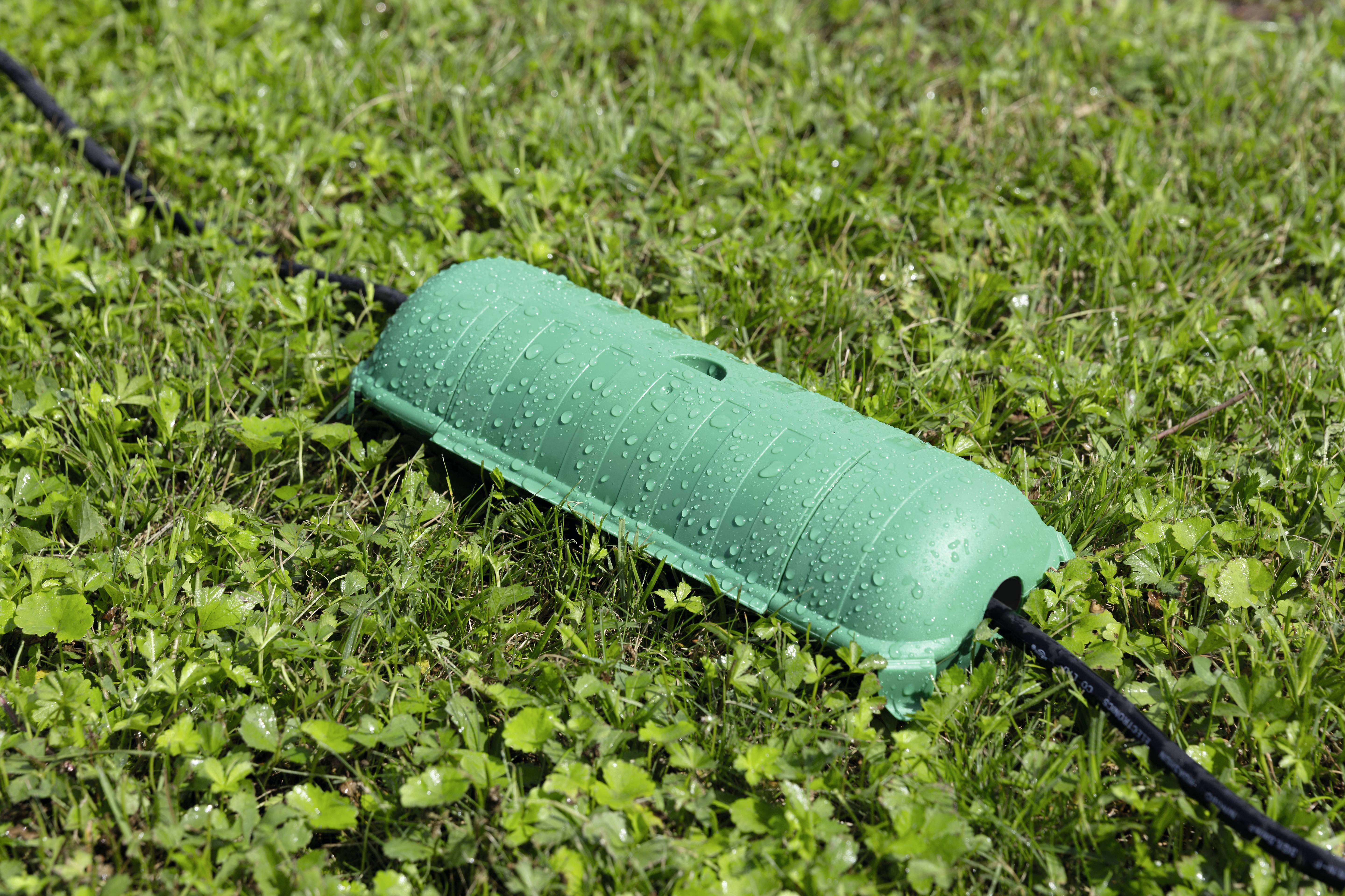 Groene kabelbeveiliging op nat gras, beschermt elektrische kabels tegen vochtigheid en weersinvloeden.