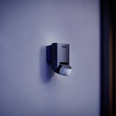 Wandgemonteerde bewegingsdetector in modern, zwart design, bevestigd aan een blauwe muur.