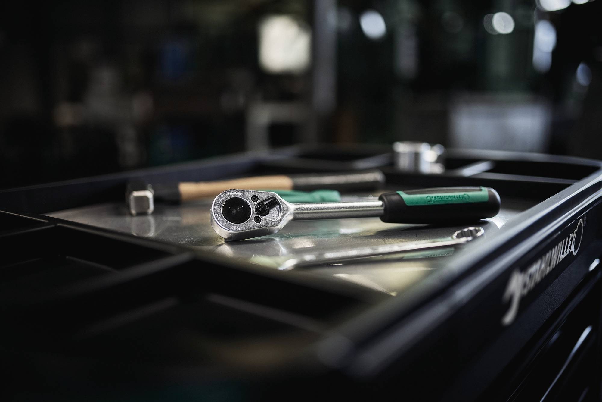 Een ratelsleutel, een dopsleutel en een schroevendraaier op een werkbankblad, wat een omgeving suggereert die gericht is op mechanisch werk of reparatie.