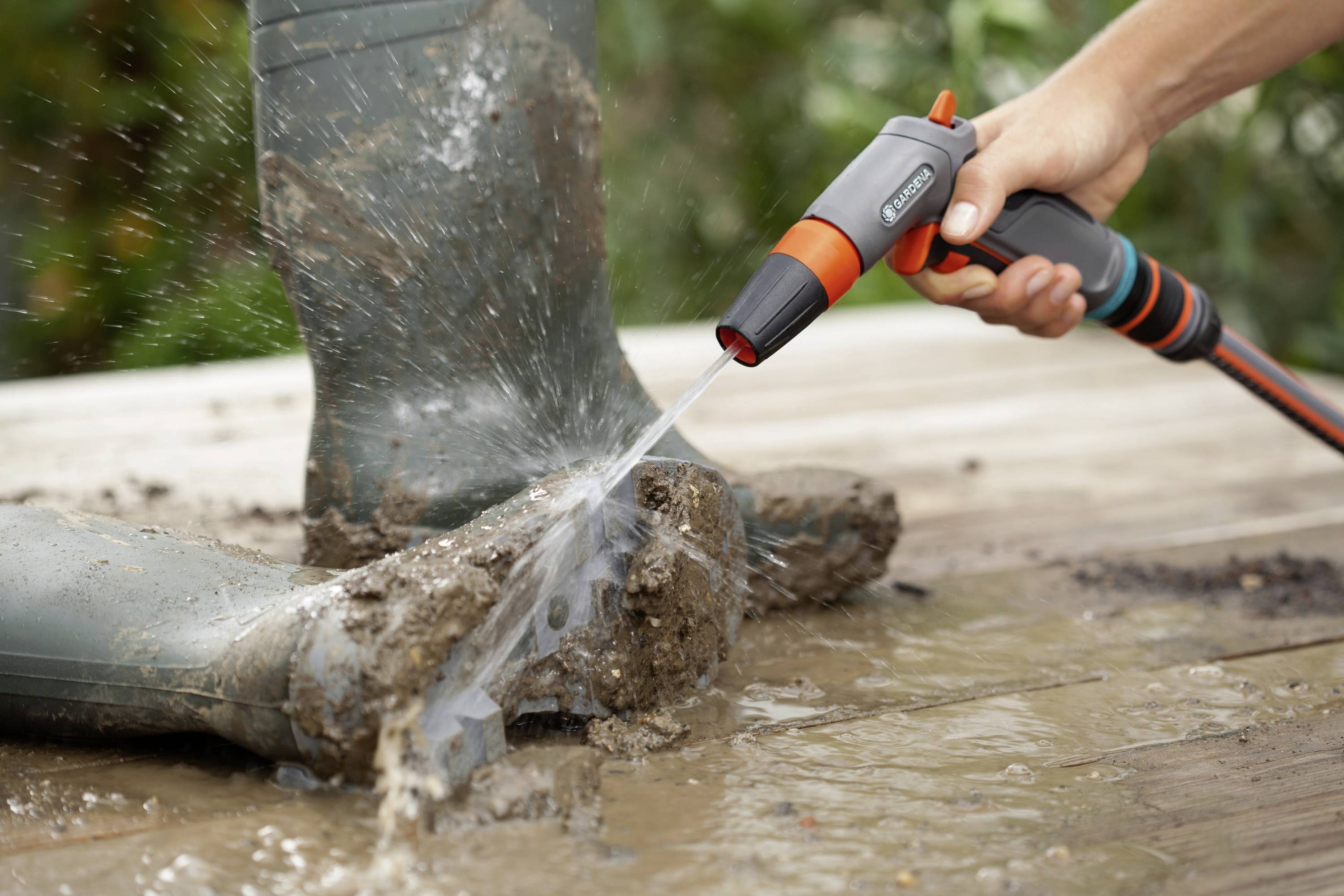 Een persoon spuit met een tuinslang water op sterk vervuilde rubberlaarzen om de aanhangende modder te verwijderen.