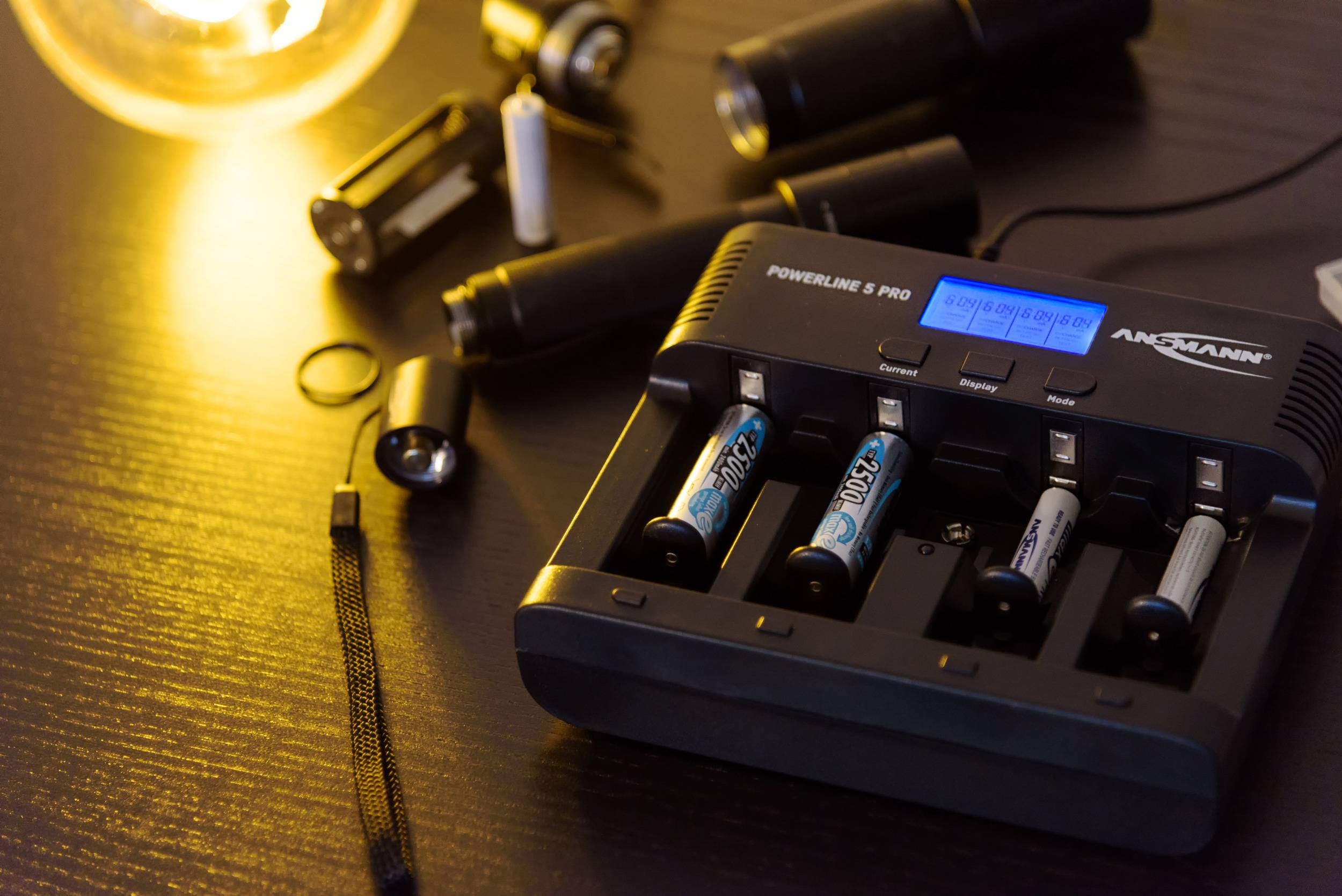 'Oplader met vier opgeladen batterijen op een tafel, omringd door zaklantaarns en een gloeilampenlicht dat warme verlichting biedt.'