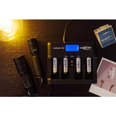 Op een tafel ligt een batterijlader met vier geplaatste AA-batterijen. Ernaast liggen twee zaklantaarns, een SD-kaarthoes en een Polaroid-foto.