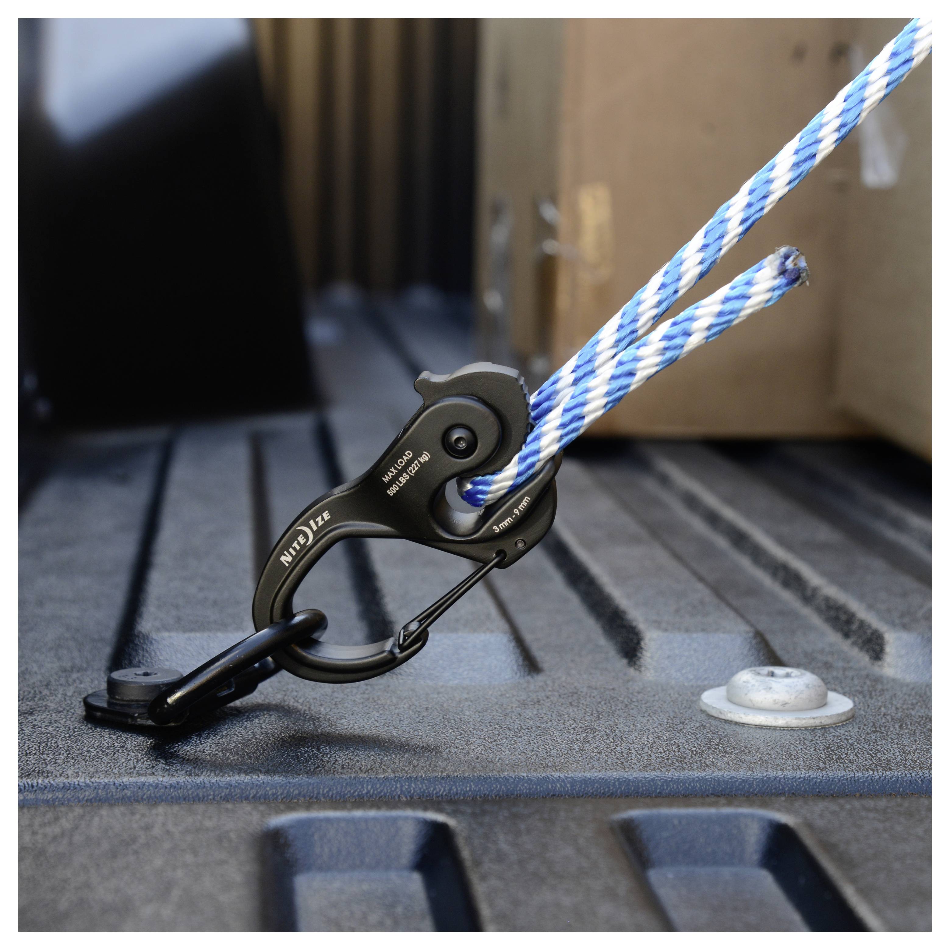 Een gestreept blauw en wit touw is stevig vastgemaakt met een metalen haak in de laadruimte van een vrachtwagen, wat suggereert dat apparatuur of lading wordt vastgebonden.