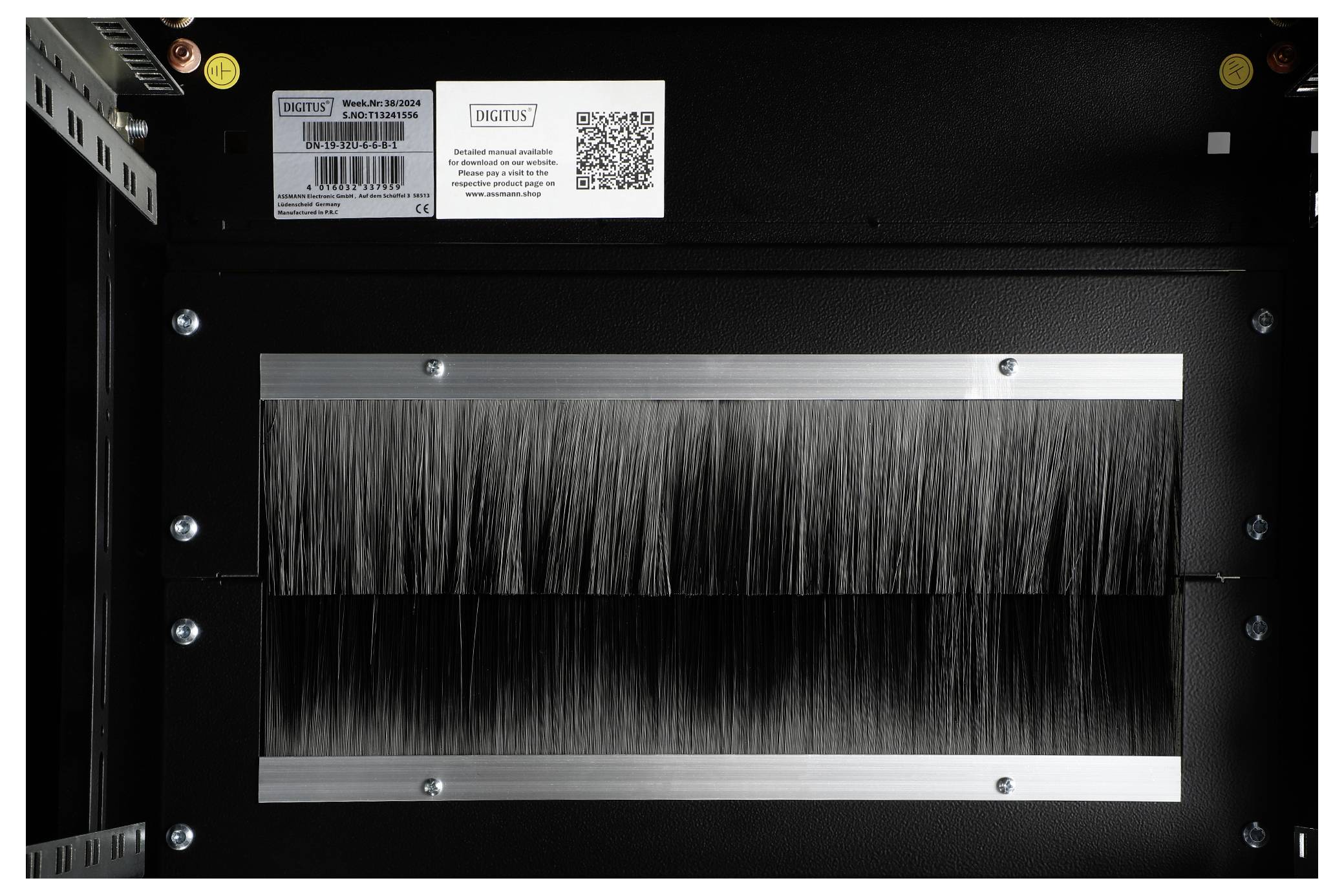 Een zwart apparaat met een metalen rail en borstels in het midden, bovenaan zijn barcode-etiketten en een QR-code zichtbaar.