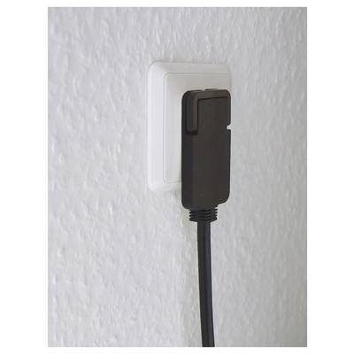 Zwarte stroomadapter aangesloten op een wit wandcontactdoos op een gestructureerde muur