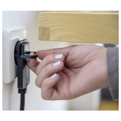 Hand die een stroomkabel uit een stopcontact in de muur onder een houten plank uittrekt.