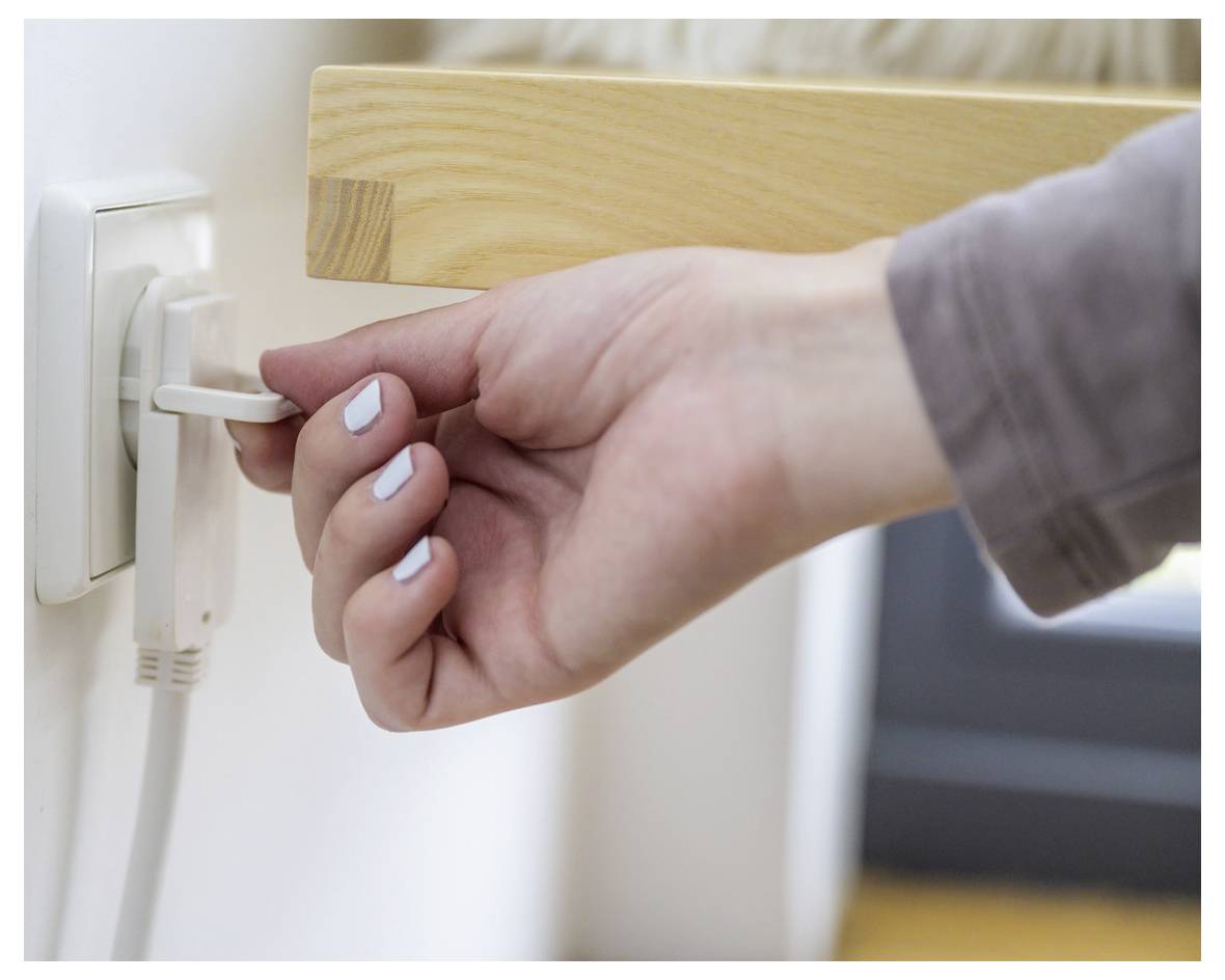 Hand die een wit apparaat in een wandcontactdoos naast een houten tafel stopt.