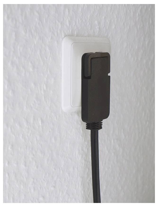 Zwarte stroomadapter ingestoken in een wit wandcontactdoos op een gestructureerde muur.