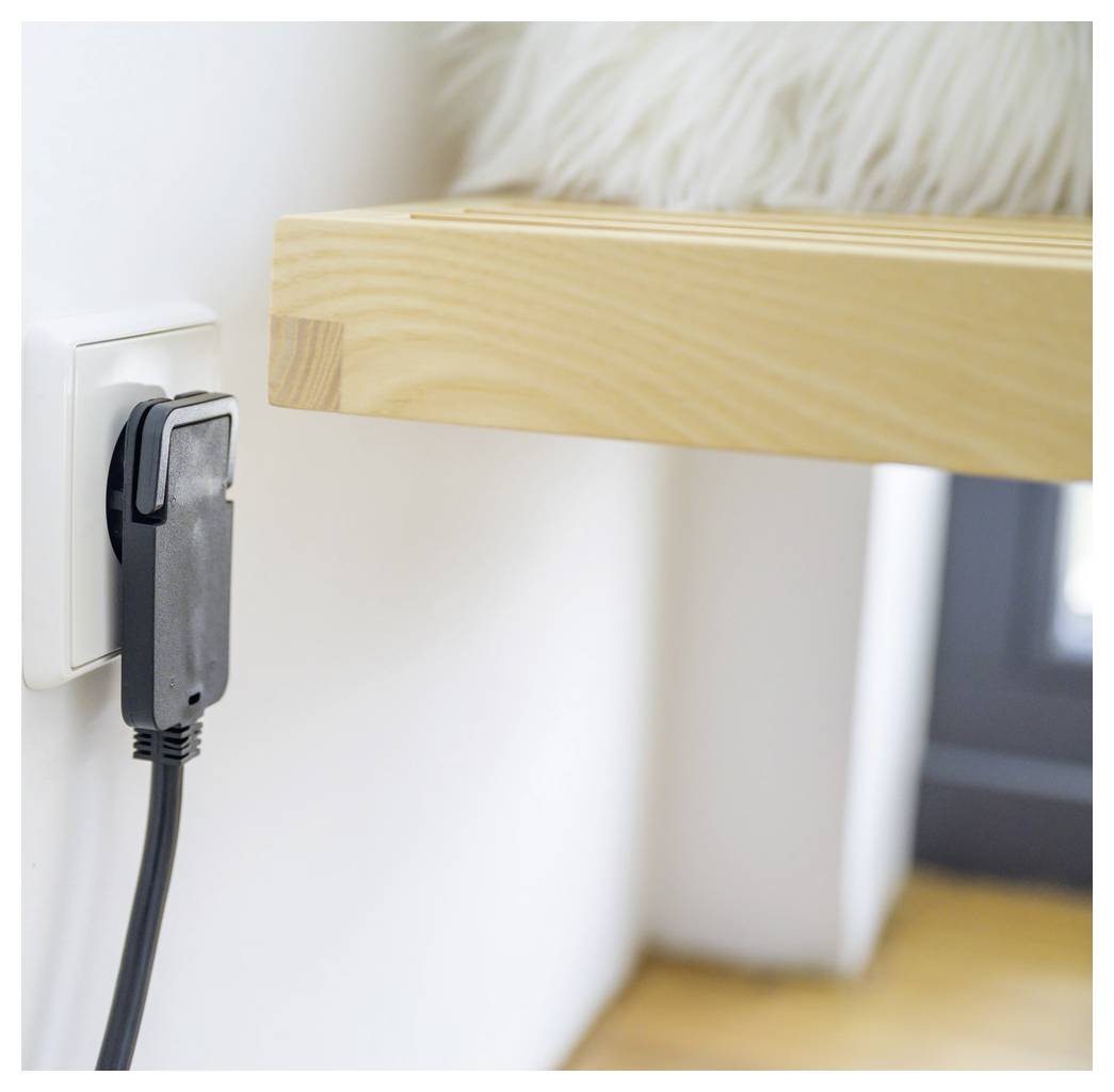 Close-up van een zwarte stekker die in een wandcontactdoos naast een houten tafelblad is gestoken, met een aangesloten stromsnoer zichtbaar in een kamer.