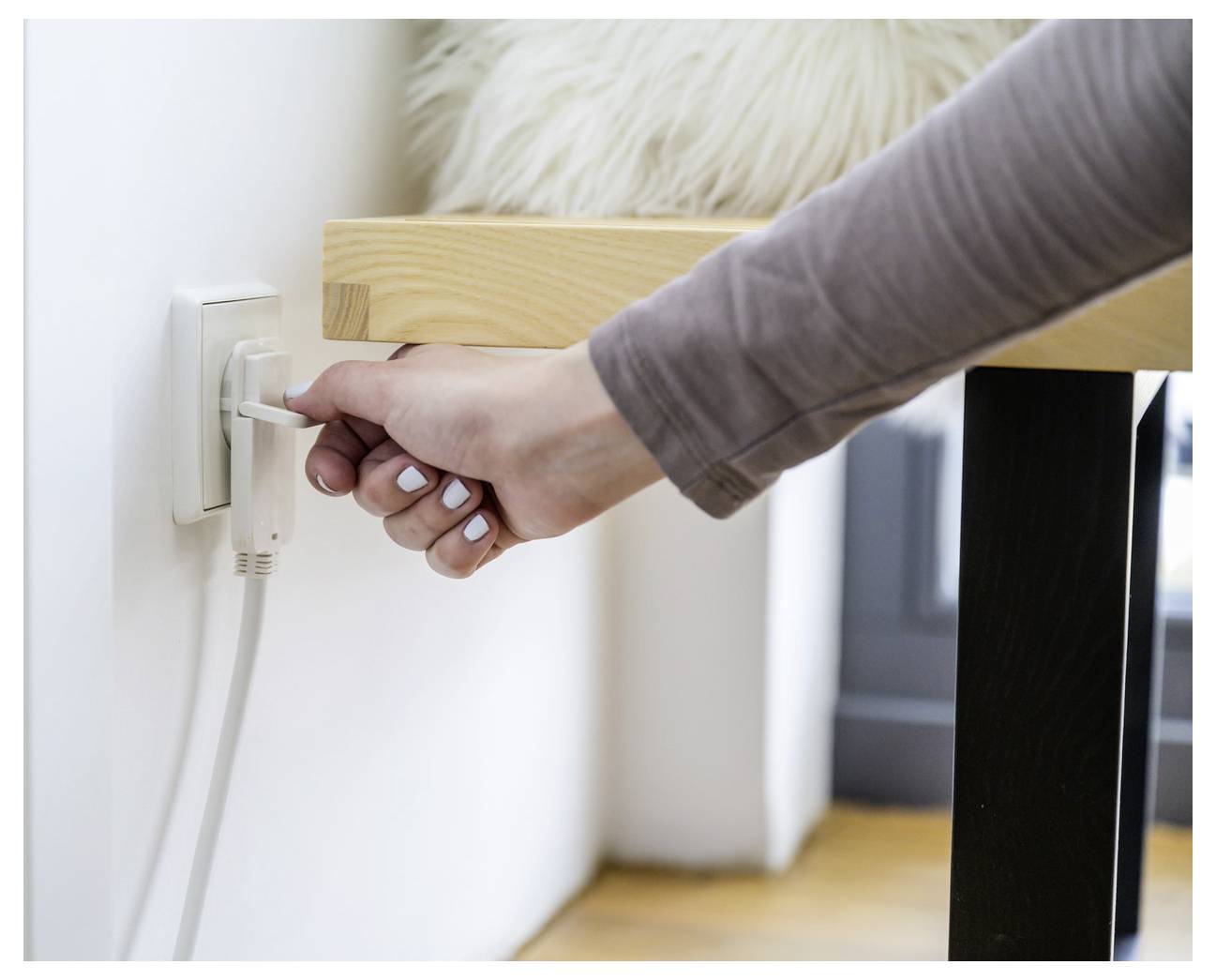 Hand die een stroomkabel in een stopcontact naast een bedframe steekt.
