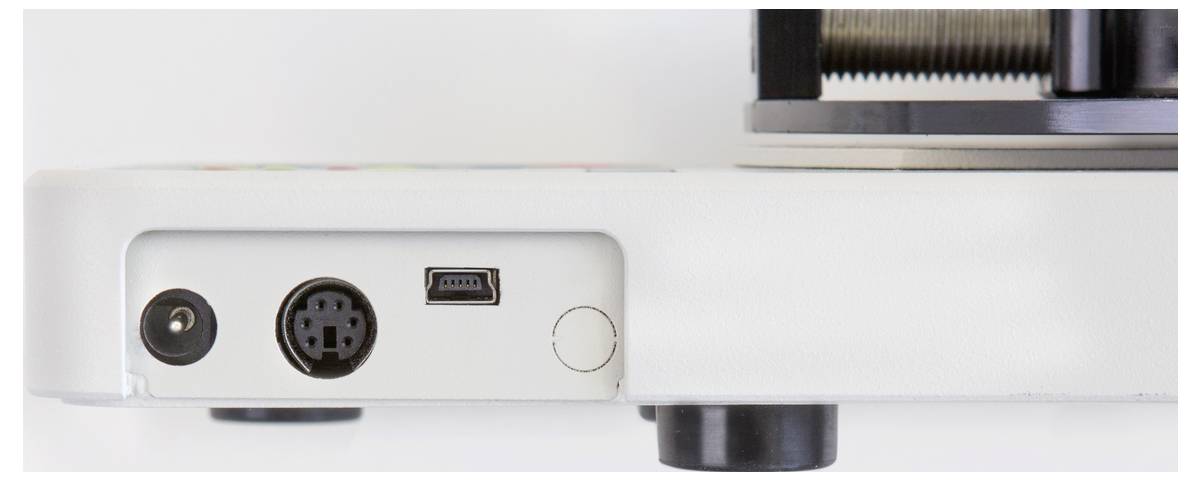 Achterkant van een elektronisch apparaat met meerdere aansluitingen: stroomaansluiting, ronde 5-pins aansluiting, Mini-USB en ronde drukknop.