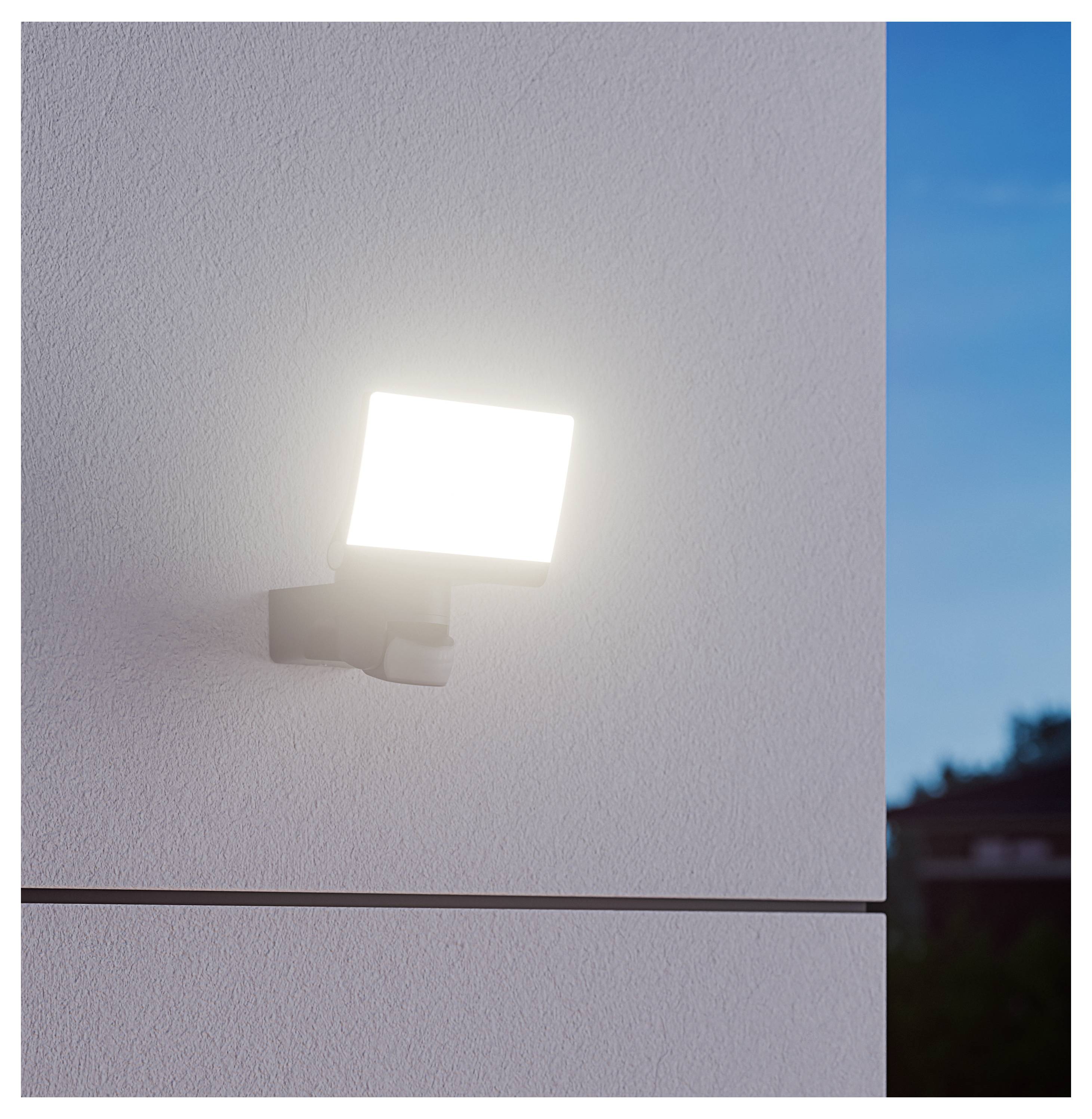 Helder aan de muur gemonteerd buitenlicht op een gestructureerde witte gebouwgevel bij schemering, met een blauwe lucht zichtbaar aan de rechterkant.