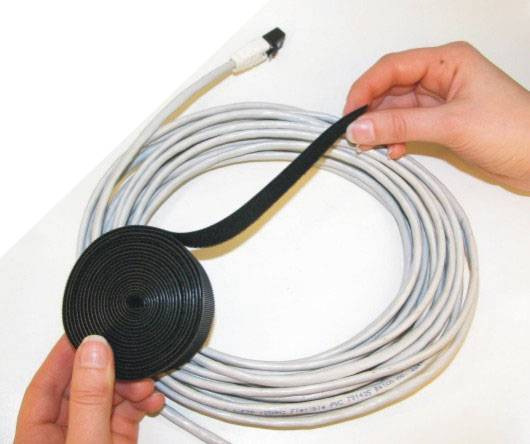 'Twee handen rollen een lang, wit kabel met een zwarte klittenband op om het te organiseren of op te bergen.'