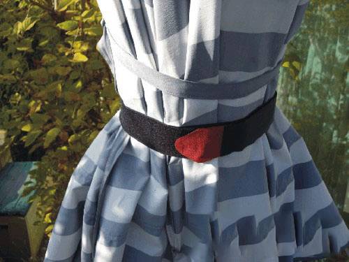 Een blauw-wit gestreepte jurk met een zwarte riem en een rode accento, hangt buiten voor herfstelijk gebladerte op de achtergrond.
