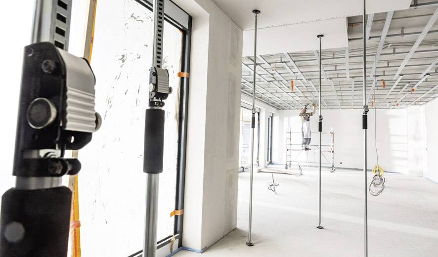 'Binnenaanzicht van een gebouw in renovatie, met plafondsteunen en een arbeider op een steiger die aan het plafond werkt.'