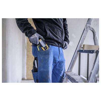 Bouwvakker in handschoenen en blauwe werkbroek houdt een draagbare lasermeter op zijn taille naast een ladder binnenshuis.