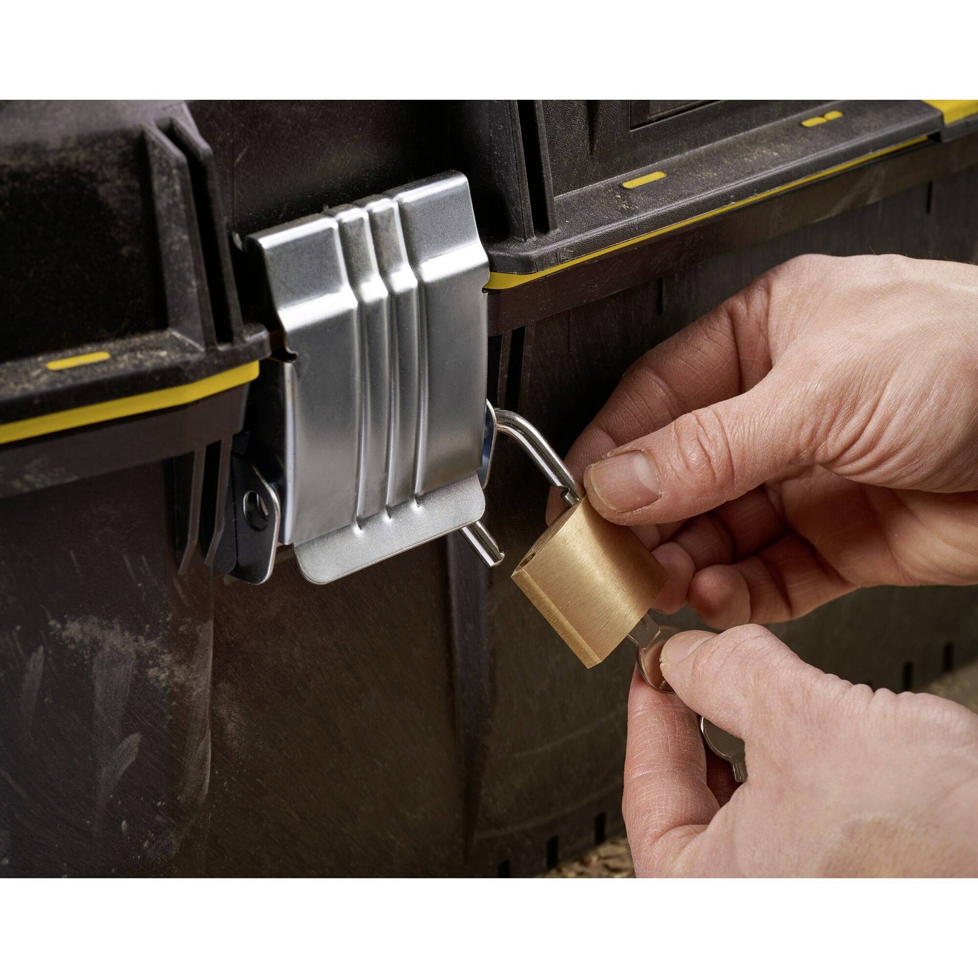 Een persoon bevestigt een hangslot aan een metalen doos. Handen houden het slot vast, dat wordt aangebracht op een slot van de doos.