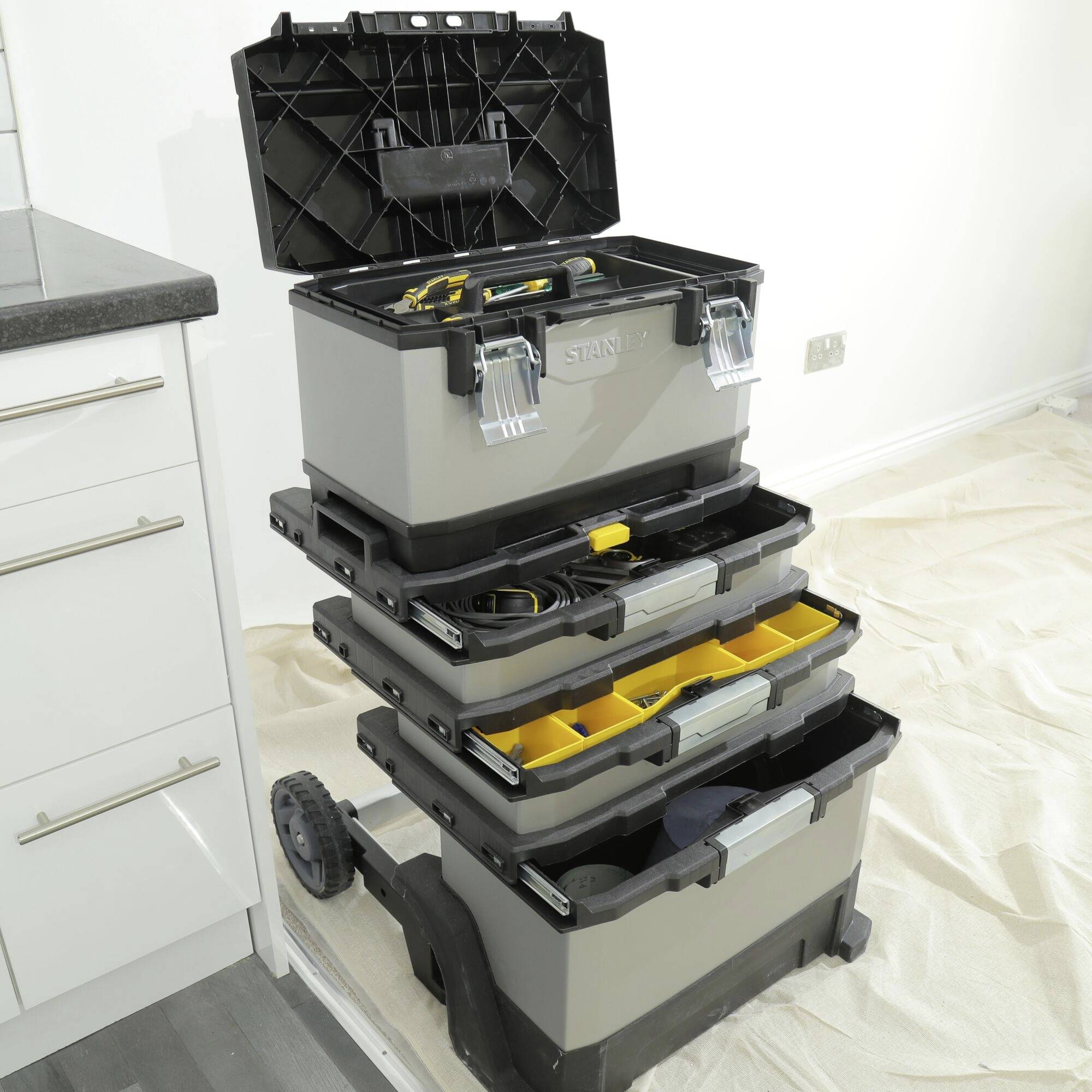 Gereedschapskist met meerdere uittrekbare vakken, gevuld met handgereedschap, staat in een keuken op een zeil.