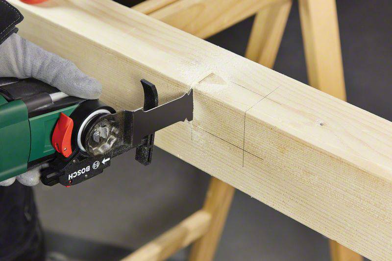 Een persoon zaagt nauwkeurig in een houten balk met een elektrische zaag, terwijl deze op een werkbank ligt.