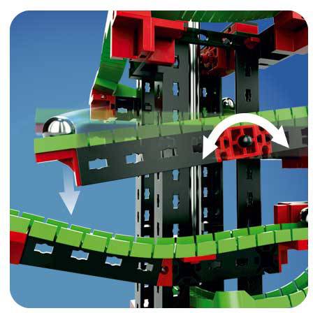 Close-up van een constructiesysteem met zwarte, groene en rode componenten. Een metalen bal rolt langs een gebogen rail.