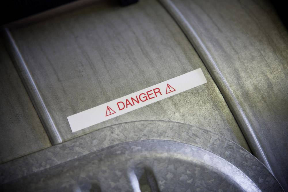 Een waarschuwingsbord met rode tekst 'DANGER' en gevarensymbolen op een metalen oppervlak wijst op mogelijke risico's.