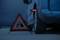 Een blauwe auto met een lekke band staat langs de kant van de weg. Een gevarendriehoek met reflecterende randen staat voor de auto.