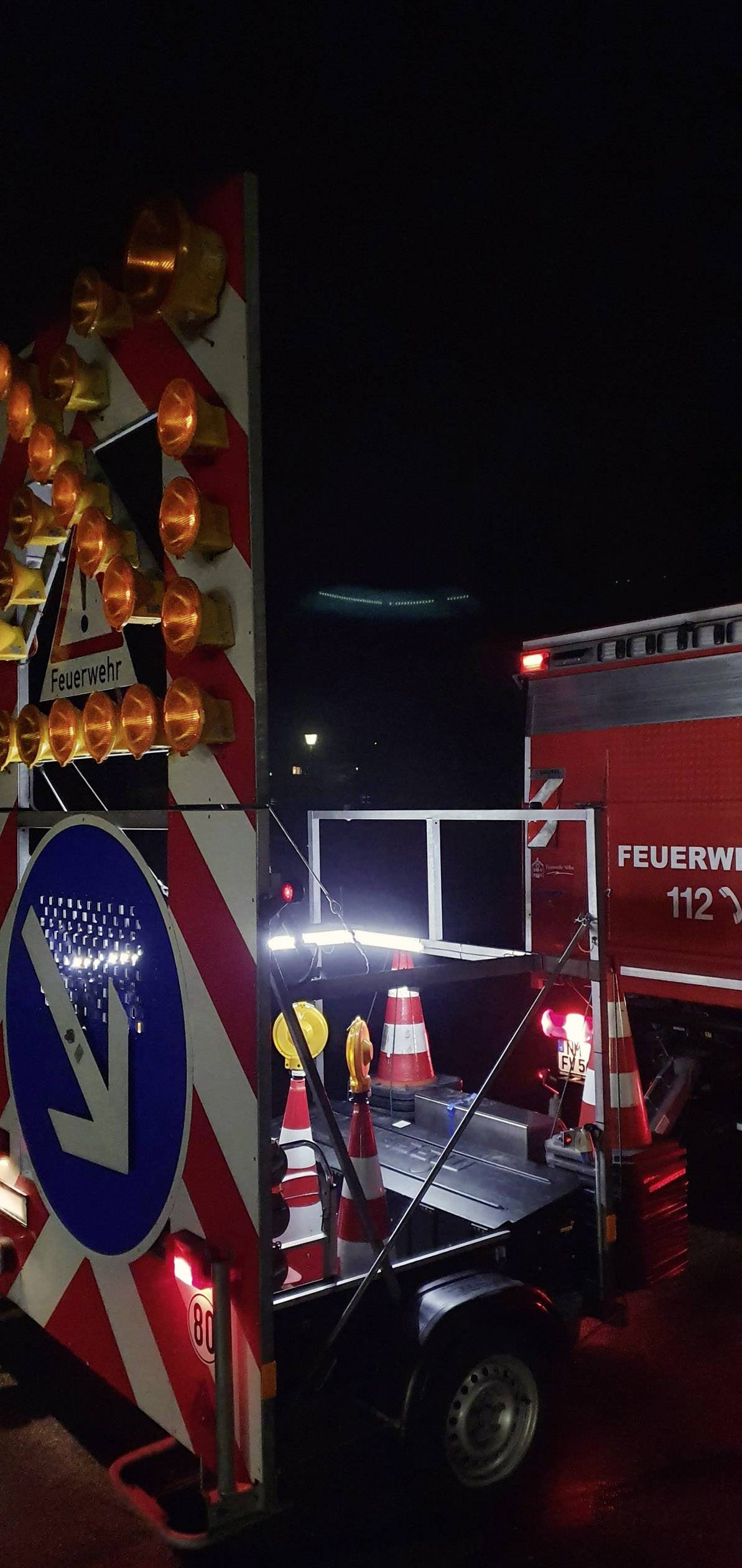 Brandweerwagen in actie 's nachts op straat. Waarschuwingsborden en -lichten wijzen op een afsluiting. Verkeersregeling zichtbaar.