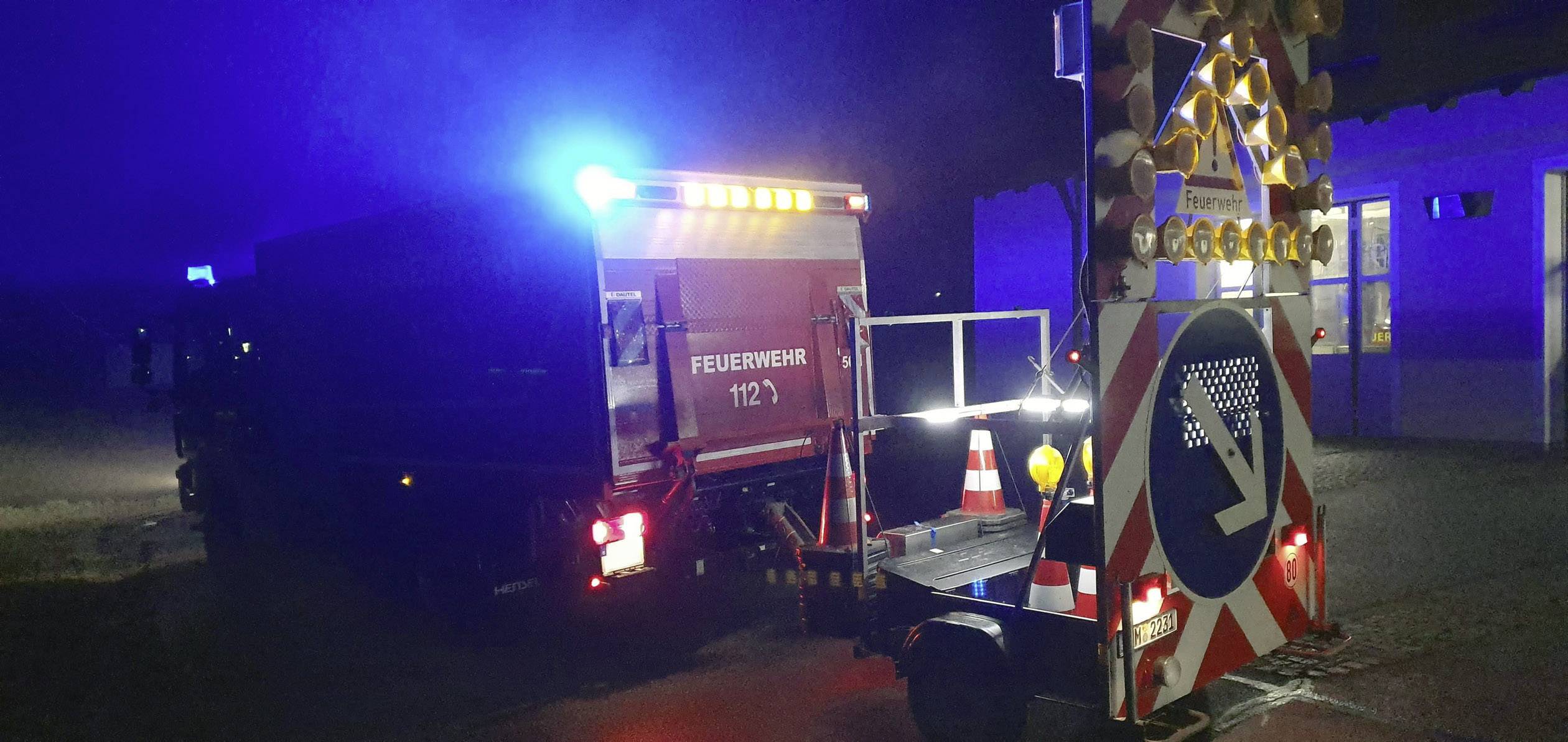 Een brandweerwagen met knipperende blauwe lichten staat 's nachts op een weg. Een aanhanger met een richtingspijl wijst naar rechts.