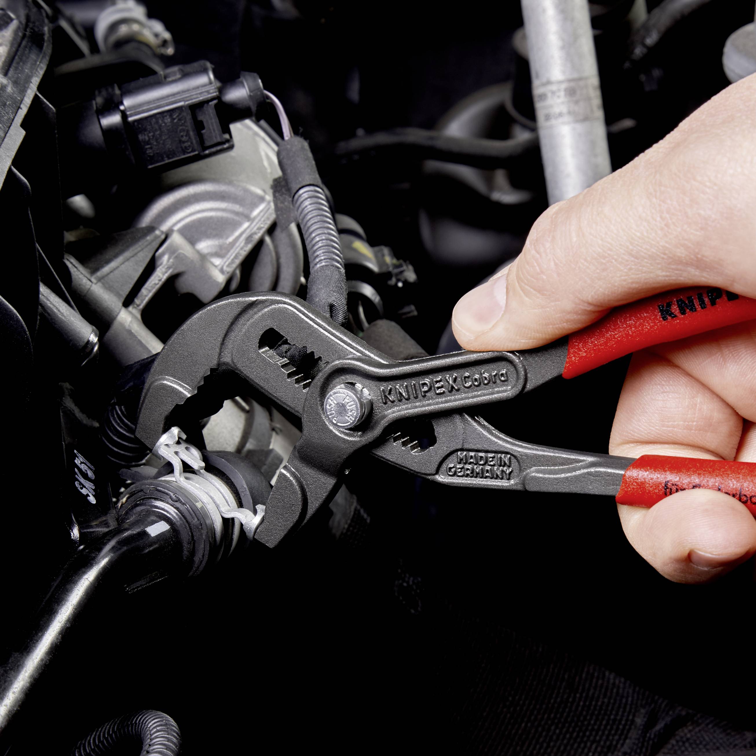 Hand houdt Knipex tang vast, die aan een buis werkt. De scène toont het gebruik van gereedschap voor mechanische werkzaamheden.